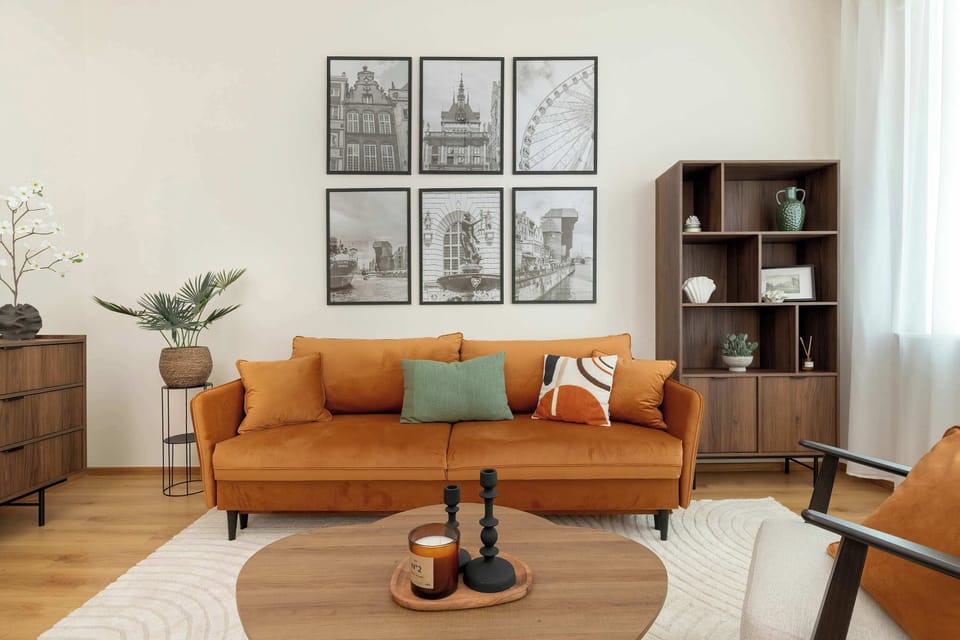 A bright living room with an orange sofa, coffee table, and wall art. The space feels modern and cozy.