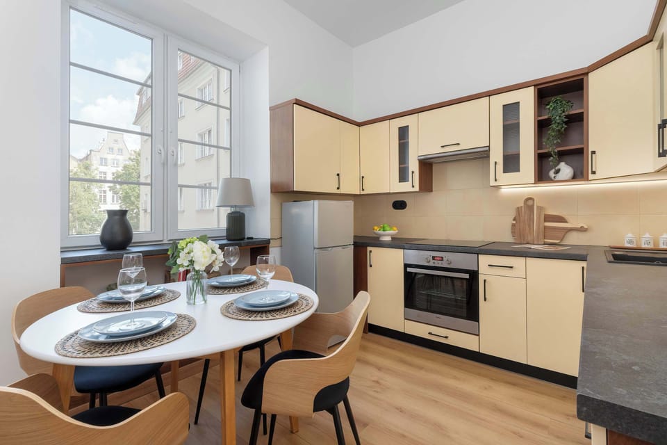 A bright kitchen with a dining table set for a meal. Large windows provide plenty of natural light.