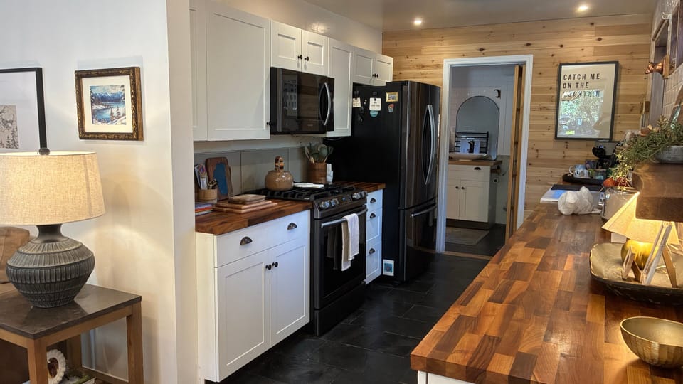 Kitchen with range, microwave, refrigerator, long counter, upper cabinets, and doorway to the utility area.