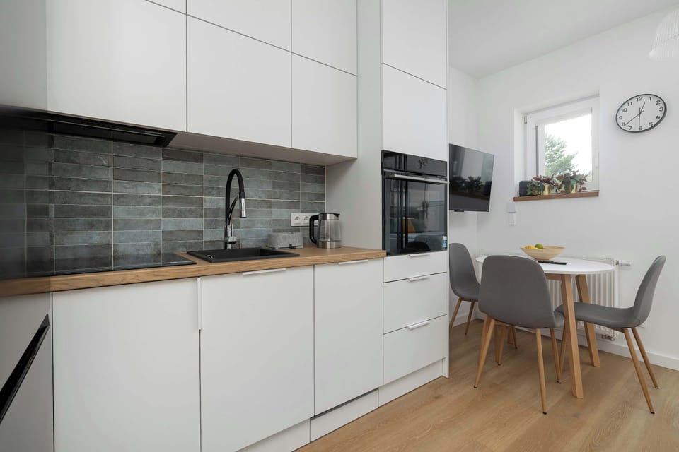 A kitchen workspace stretches along the wall with integrated appliances and dark backsplash tiles. Minimalist finishes emphasize functionality.