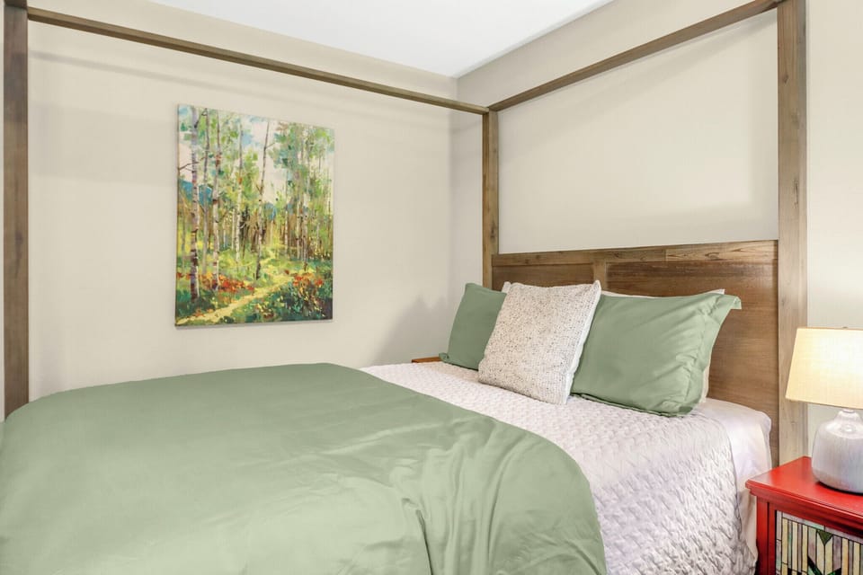Slip into crisp linens and soft sage-green bedding in your tranquil bedroom, where natural wood tones and soothing forest artwork set the scene for restful nights.