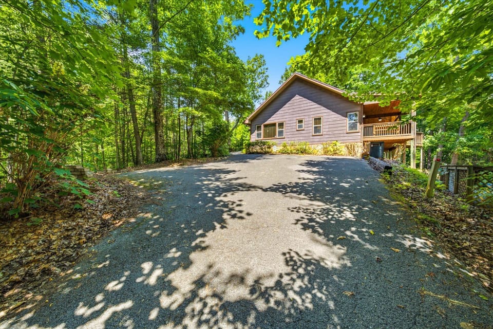 Nestled in a lush forest, this private mountain retreat offers a spacious driveway and peaceful natural surroundings, framed by vibrant greenery and summer sunshine.