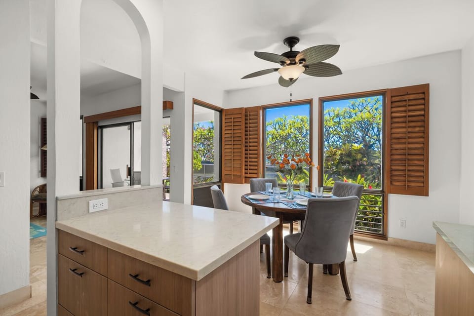 Enjoy your morning coffee at this sunny dining spot, where lush tropical views frame every meal and cool breezes flow through. The open kitchen island makes gathering effortless.