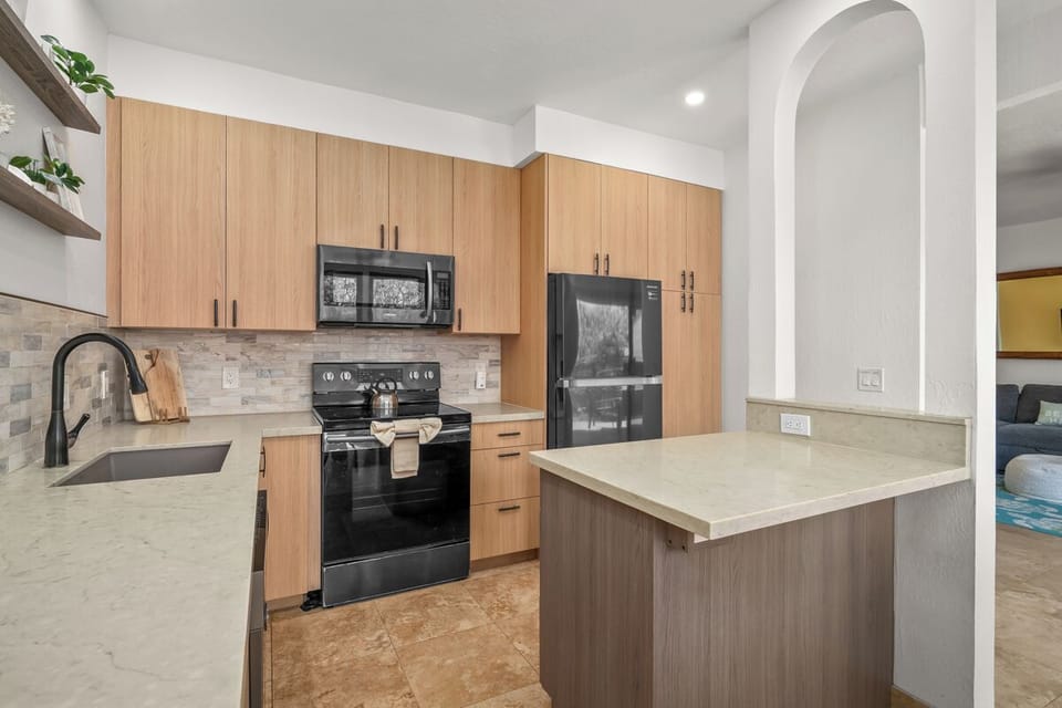 You'll love preparing meals in this modern kitchen featuring sleek light wood cabinetry, elegant stone countertops, black stainless appliances, and plenty of space to create culinary masterpieces during your stay.