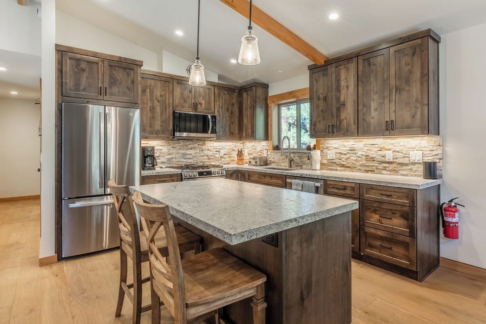 A beautiful mountain-inspired kitchen features rustic wood cabinetry, modern stainless appliances, and a spacious granite island perfect for gathering over morning coffee or preparing meals during your stay.