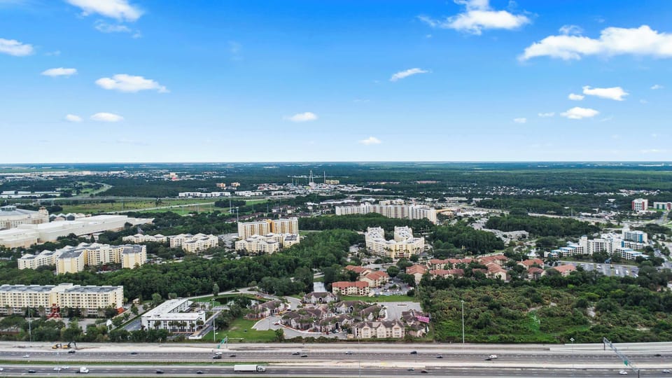 Sweeping aerial view of the surrounding area under a bright blue sky w/ open roads & lush greenery all around.