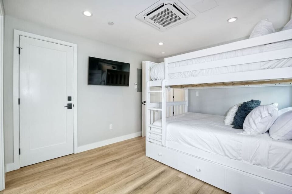 BEDROOM #2 – Second-Floor Bunk Room with TV Features full-size bunk beds and a flat-screen TV, offering a comfortable and flexible sleeping space that’s perfect for kids, teens, or additional guests in this spacious beach house just steps from the ocean.