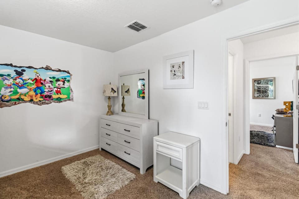 Children's bedroom corner with beige carpet, white dresser and mirror, butterfly lamp, and colorful cartoon wall decal.