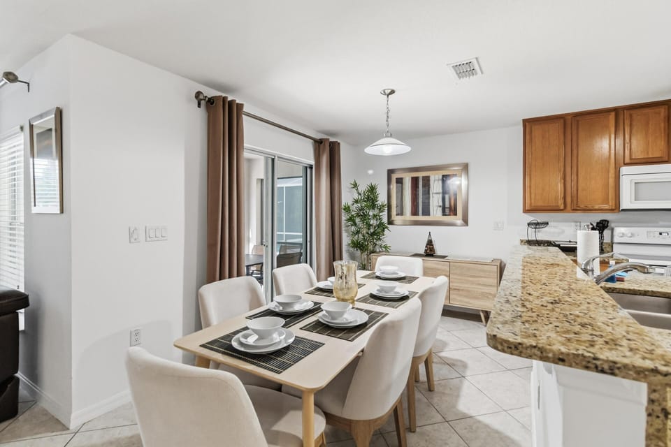 Dining area with light wood table set for six, beige upholstered chairs, and sliding glass doors with brown curtains.