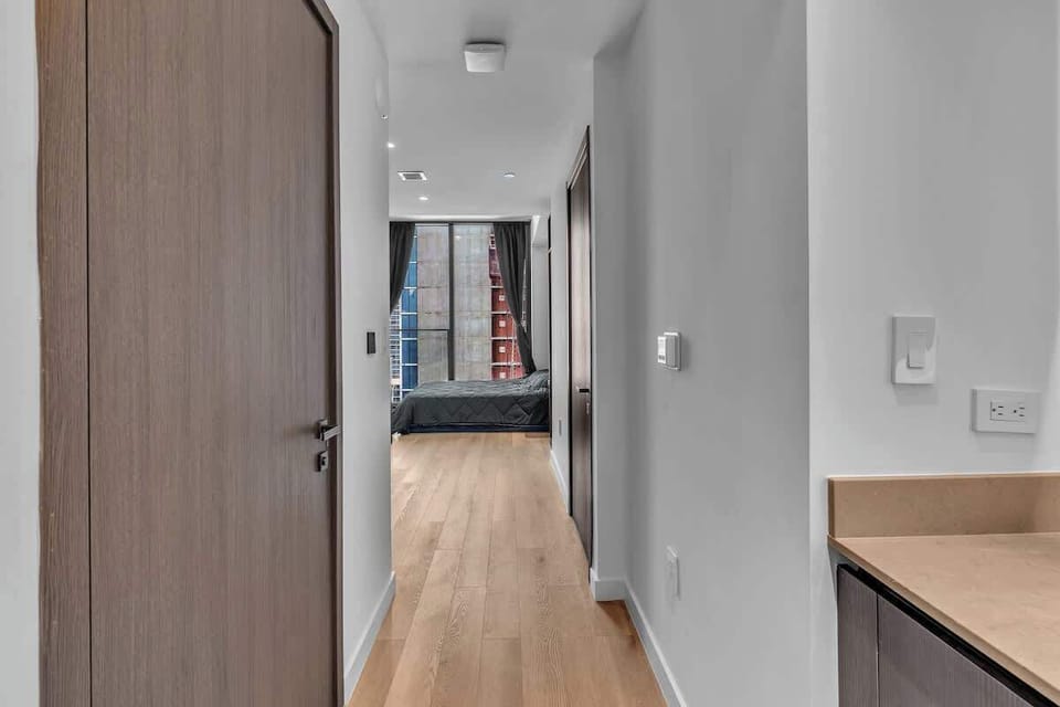 Welcoming entryway with warm wood floors leading into a bright, modern living space. Clean lines and a sleek design create an inviting flow, while floor-to-ceiling windows and city views await just beyond the hallway.