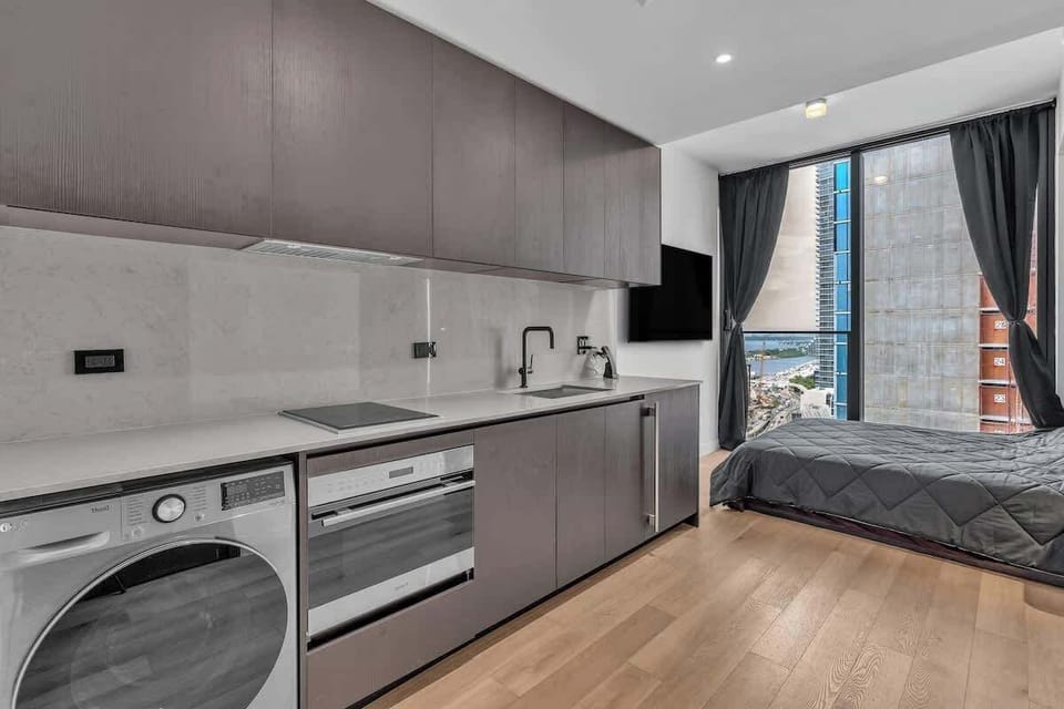 Modern studio with sleek European-style kitchen, full-size washer/dryer, oven, and cooktop. Bright living space with floor-to-ceiling windows, plush bedding, and stunning city views. Stylish, efficient, and move-in ready in the heart of it all.