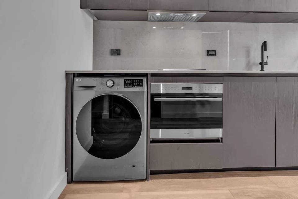 Modern kitchen featuring a full-size washer/dryer, built-in oven, and sleek cooktop with overhead range hood. Stylish cabinetry and clean contemporary finishes make this fully equipped space ideal for cooking and everyday convenience.