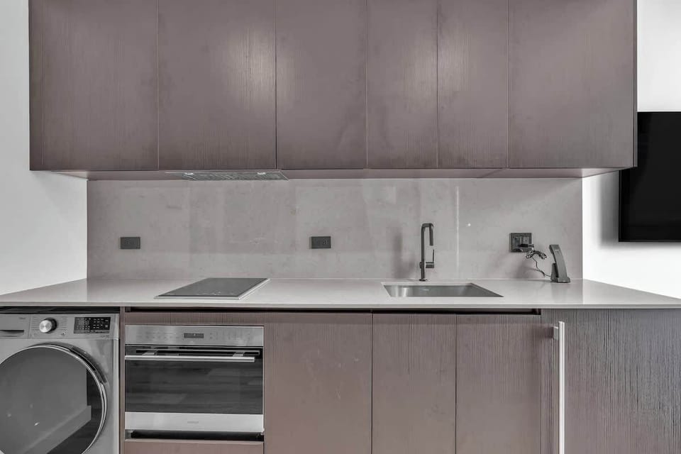 Fully equipped modern kitchen with sleek cabinetry, full-size washer/dryer, built-in oven, cooktop, and stainless sink. Clean lines and a bright backsplash create a stylish, functional space for cooking and everyday convenience.
