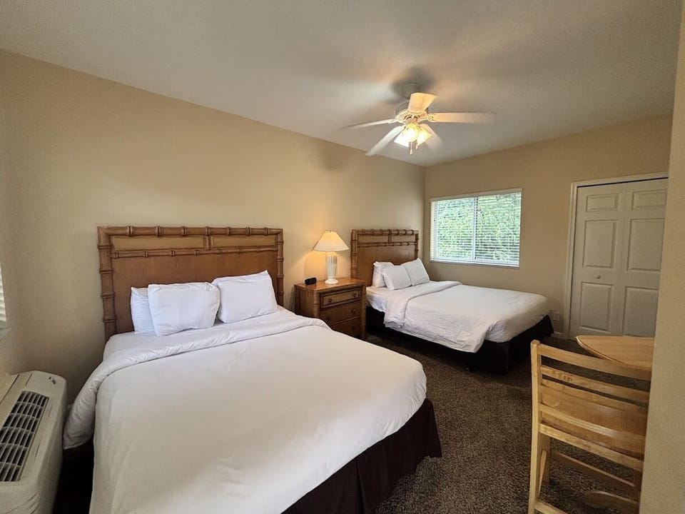Comfortable bedroom with two beds, ceiling fan, bedside lighting, and a convenient in-room dining/work space.