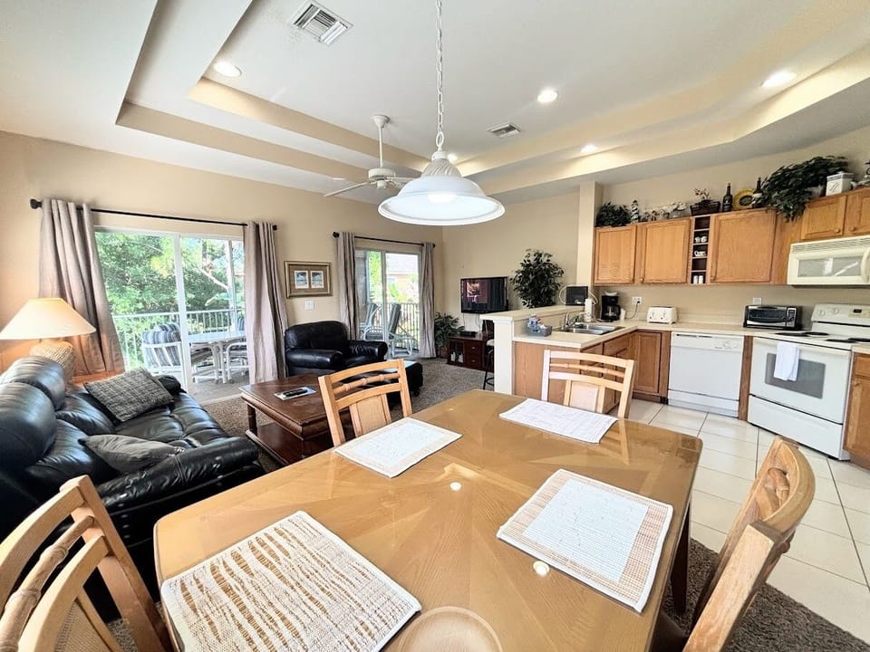 Open dining, kitchen, and living space with tray ceilings, comfortable seating, and a bright, welcoming layout