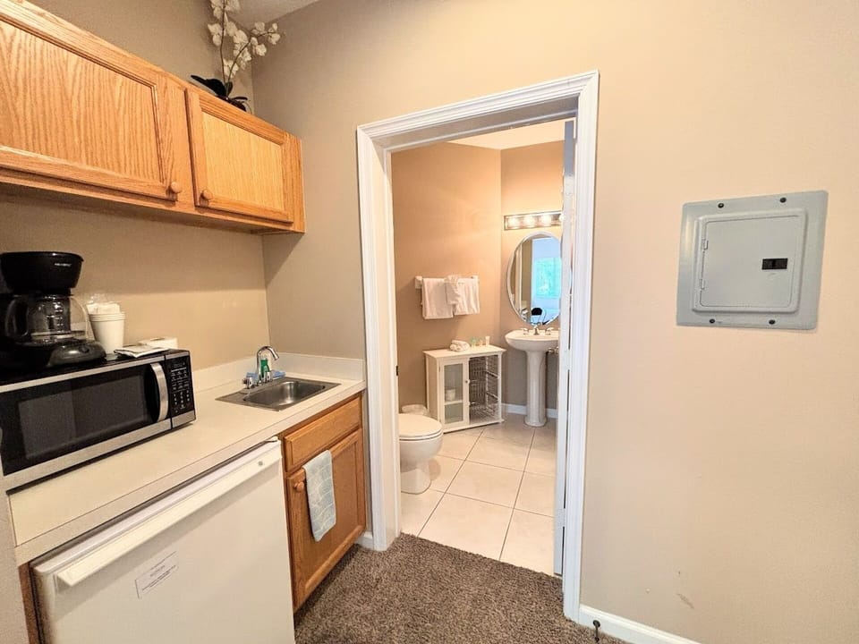 Functional kitchenette space with microwave, mini fridge, coffee maker, sink, and easy access to the bathroom.