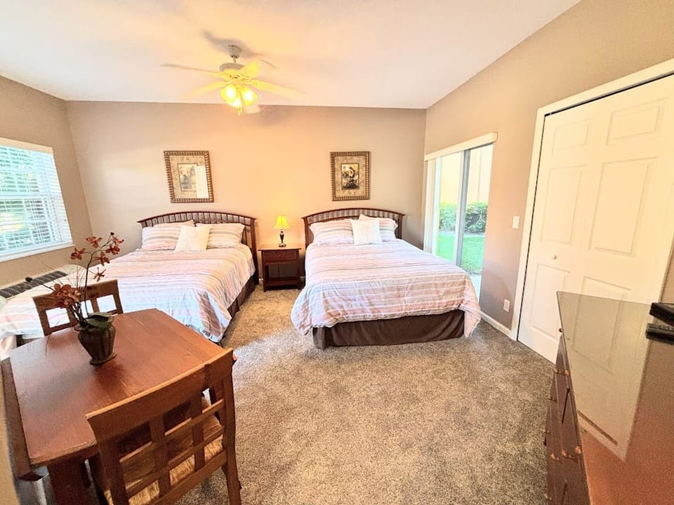 Bright bedroom featuring two beds, ceiling fan, dresser storage, and a cozy table with seating.