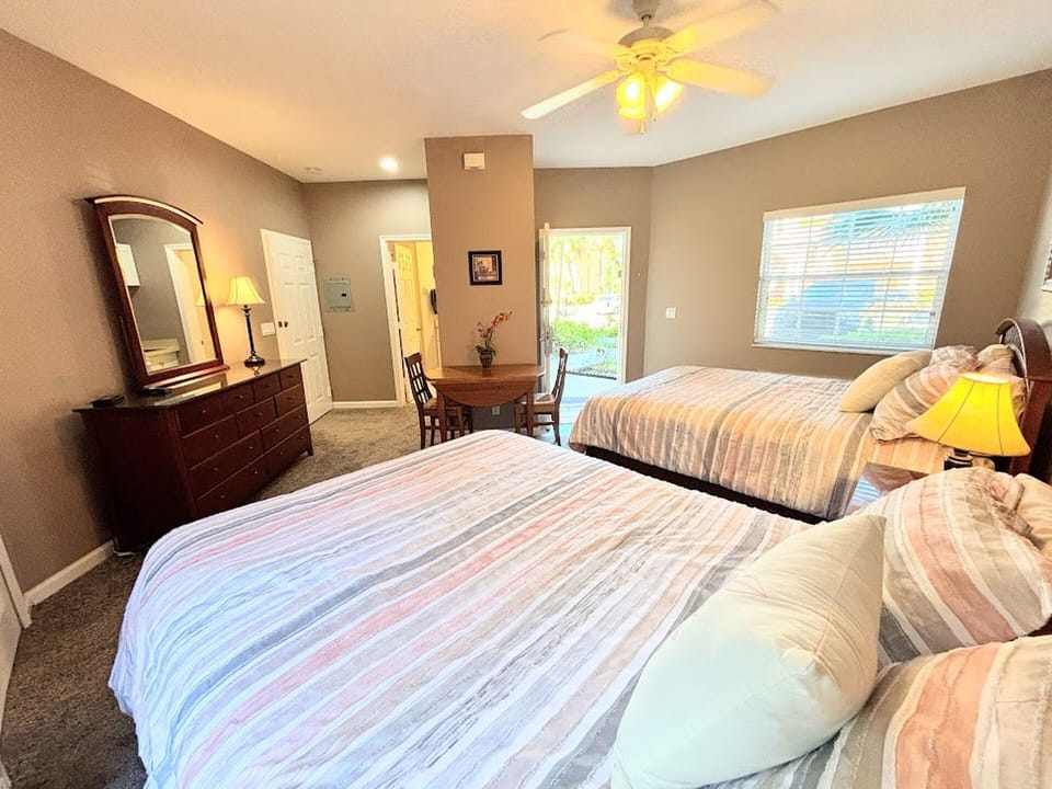 Comfortable bedroom layout with two beds, dresser storage, small dining/work area, and easy access to the bathroom.