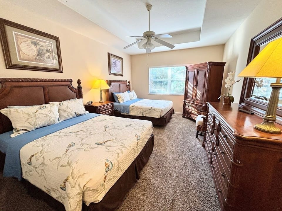 Spacious bedroom featuring two comfortable beds, ceiling fan, ample dresser storage, and warm natural light for a relaxing stay.