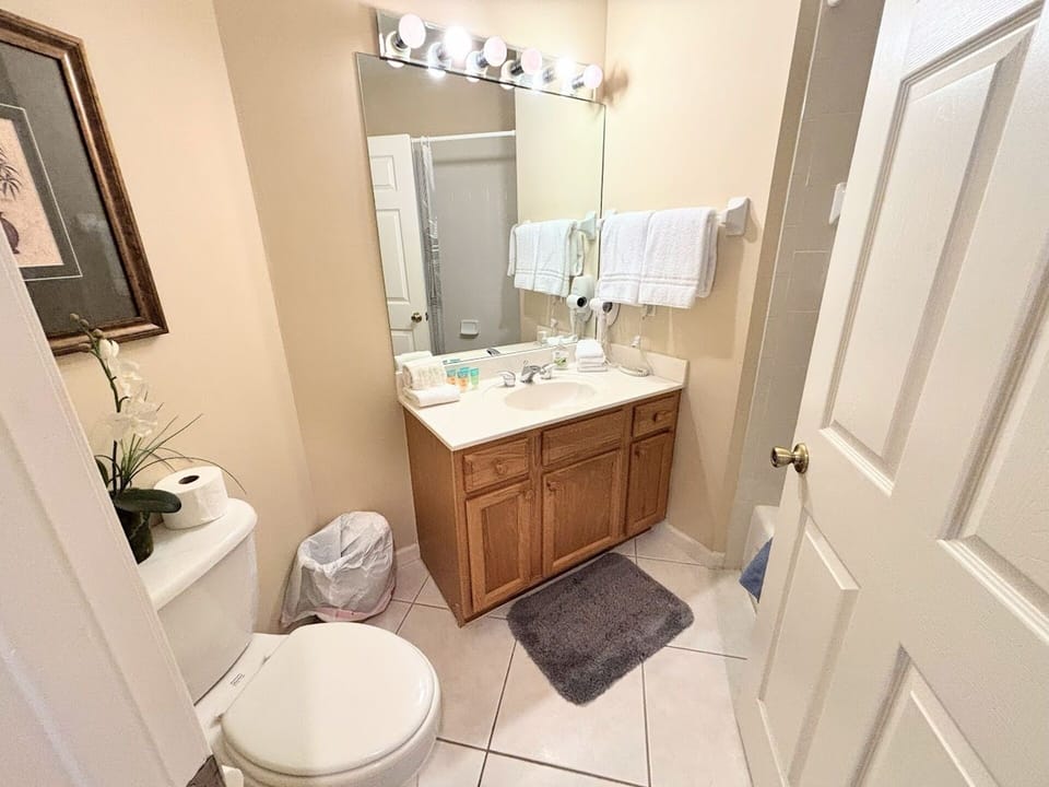 Clean bathroom with vanity storage, tile flooring, toilet, and bright mirror lighting.