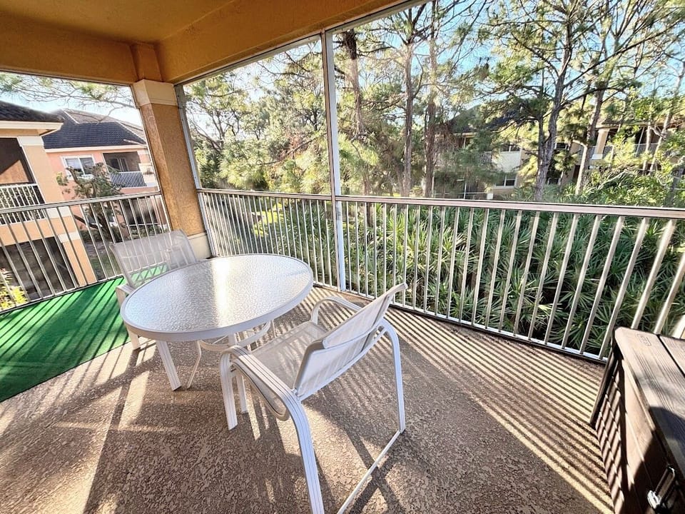 Spacious screened balcony with outdoor dining space and relaxing views of the landscaped surroundings.