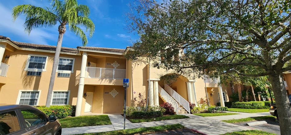 Exterior view of the building with tropical landscaping, covered entryways, and bright Florida-style architecture.