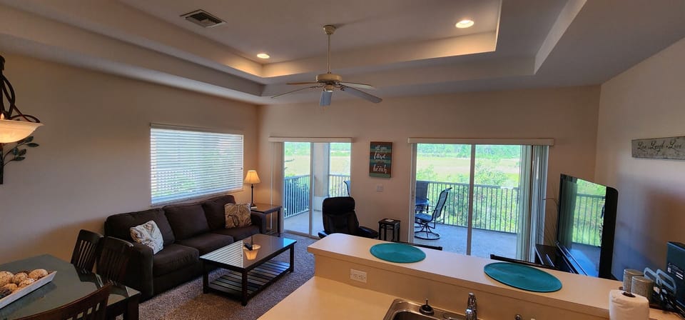 Bright living area with cozy seating, tray ceiling, and sliding glass doors leading to the screened balcony.