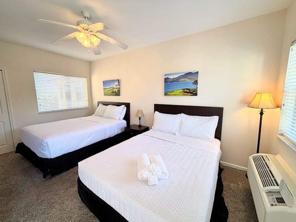 Bright bedroom with two comfortable beds, ceiling fan, bedside lighting, and a relaxing layout.