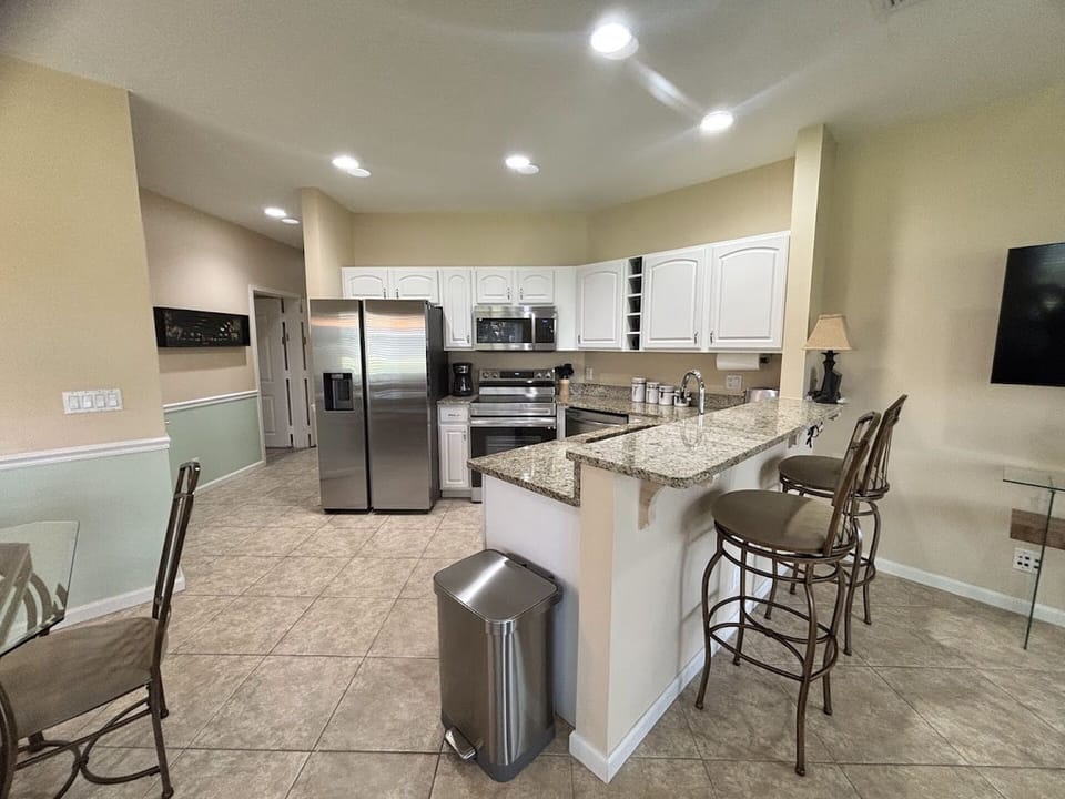 Updated kitchen with granite countertops, breakfast bar seating, stainless steel appliances, and an open view into the living area.
