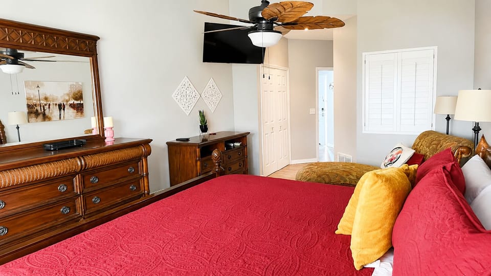 Comfortable bedroom with a large bed, dresser storage, wall-mounted TV, and a relaxing layout.
