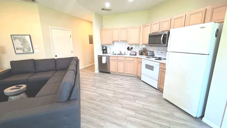 Open kitchen and living area with full-size appliances, wood-look flooring, and a comfortable sectional sofa.