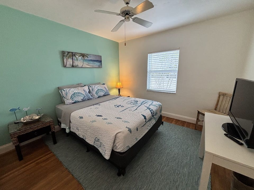 Comfortable bedroom with coastal decor, TV, wood flooring, and a relaxing beachy feel.