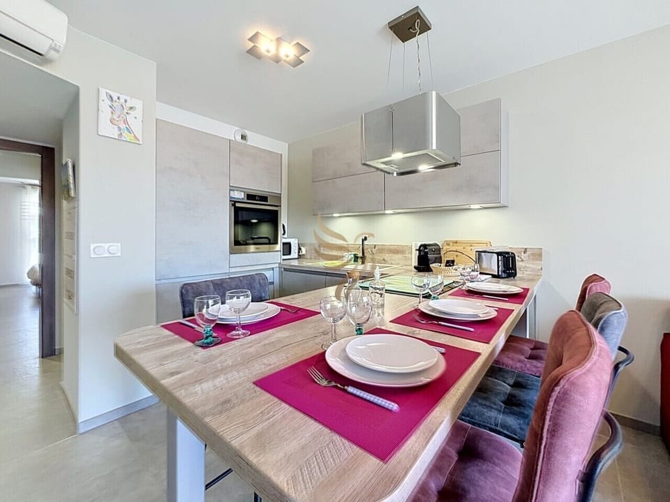 Prenez place au bar en bois, chaises velours et sets fuchsia invitent à un petit-déjeuner chaleureux. Entre hotte inox et four encastré, cette cuisine moderne promet des moments conviviaux et confortables.