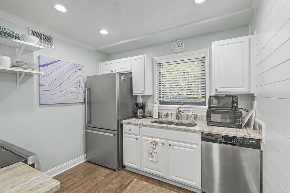 The well-appointed kitchen includes stainless steel appliances, crisp white cabinetry, and granite countertops. A drip coffee maker rests near the double sink, with a microwave and toaster oven stacked neatly beside the dishwasher.