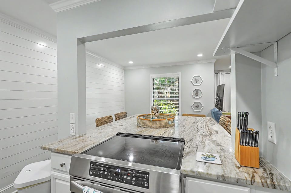 The smooth marble-look kitchen island features a built-in smooth-top electric range stove. Shiplap detailing lines the side wall, keeping the cooking space bright, open, and connected to the adjacent dining area.