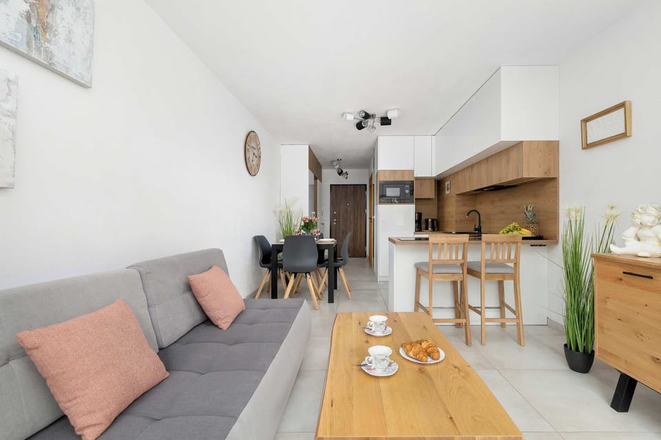 An open-plan living room and kitchenette with a sofa and dining area. The interior is bright and functional.