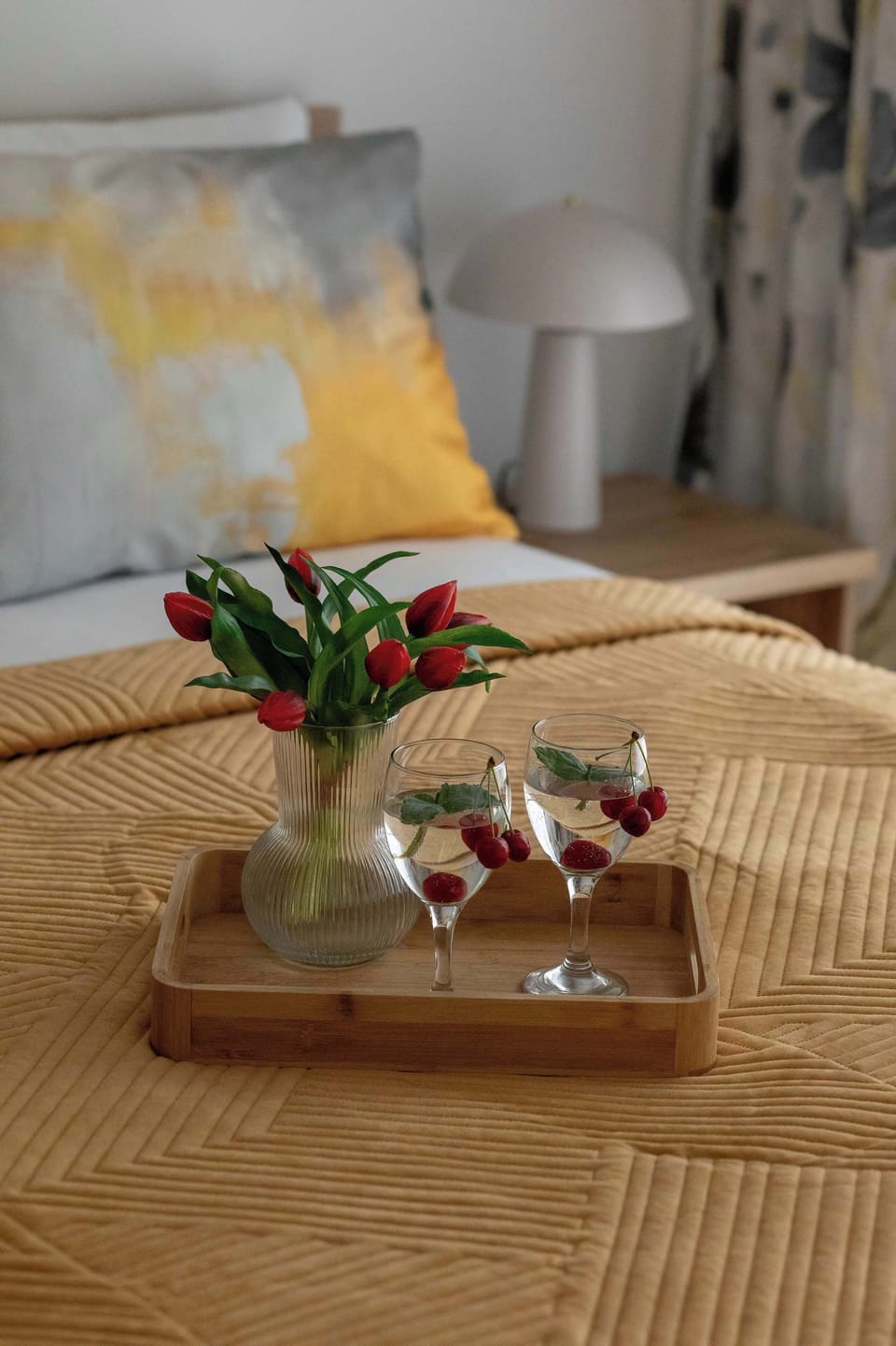 A close-up of a tray placed on the bed with elegant glasses and fresh flowers. The arrangement adds a delicate and romantic touch to the space.