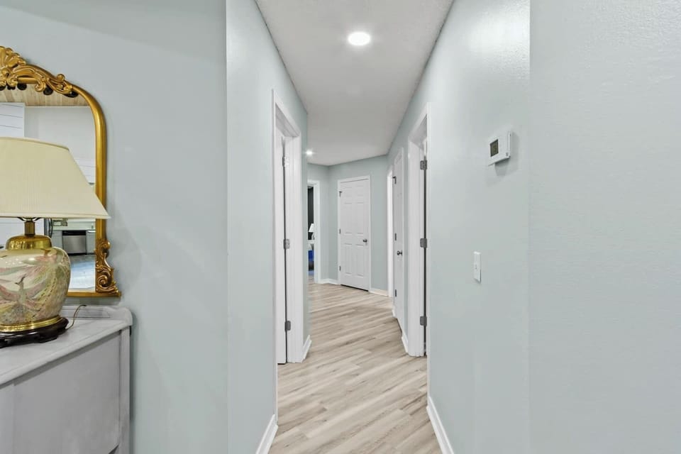 Clean, well-lit hallway with soft seafoam walls, light hardwood floors, and crisp white panel doors leading to multiple rooms. Simple, bright, and cohesive with the home's fresh coastal aesthetic throughout.