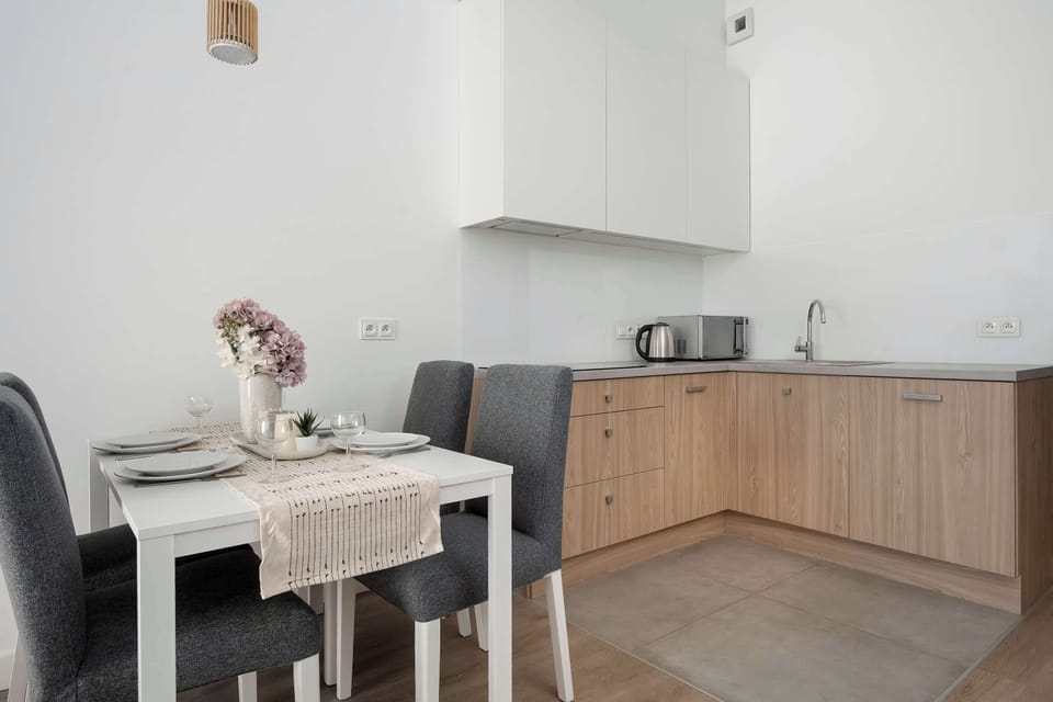 A dining nook with a small table and floral centerpiece sits adjacent to the kitchen area. Soft colors create a warm and inviting setting.
