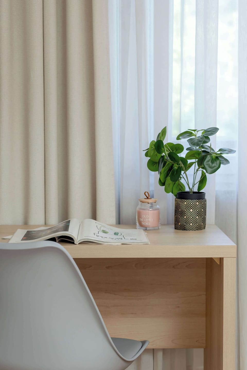 A vertical close-up shows the wooden desk area, decorated with a small green potted plant that adds a touch of nature indoors. The soft fabric curtains in the background create a warm, cozy texture.