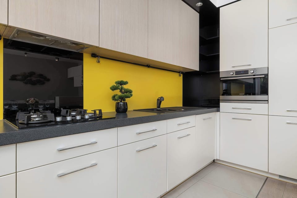 This close-up view of the kitchen highlights sleek white lower cabinetry contrasted against a vivid yellow backsplash. Modern black appliances and a dark countertop give the cooking space a clean, stylish look.