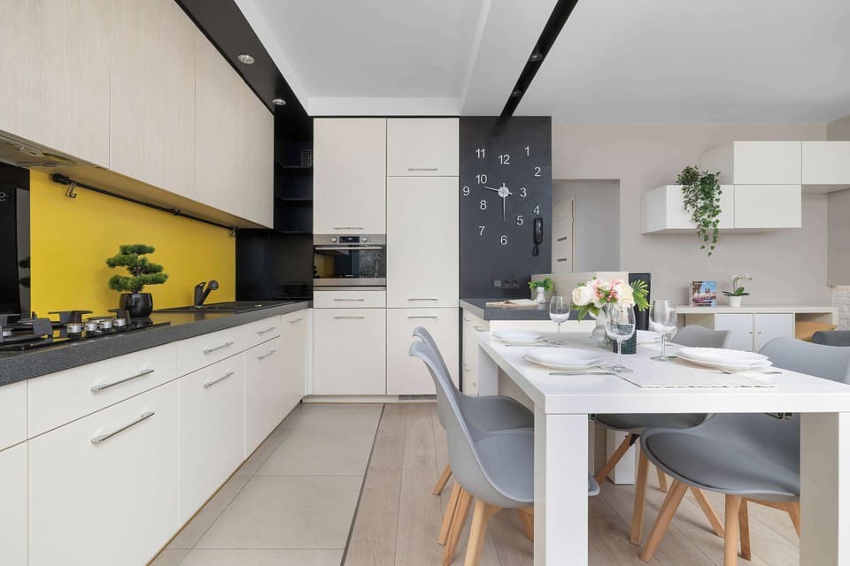 The kitchen and dining space are shown together, highlighting the smooth flow between the white cabinets and the eating area. Bright yellow walls behind the countertops inject a cheerful energy into the interior design.