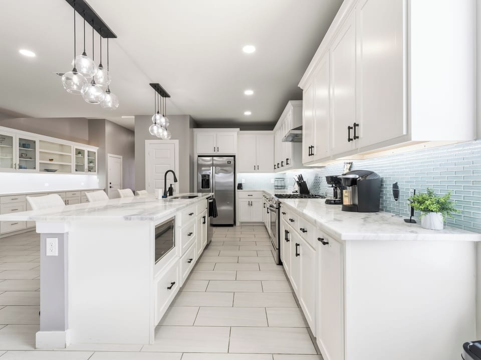 Gleaming marble countertops and a spacious center island invite you to whip up your favorite meals in this bright, fully-equipped chef's kitchen with modern appliances and coastal-inspired backsplash.