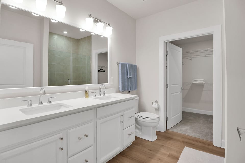Primary suite bathroom — double vanity, walk-in closet, glass-enclosed shower