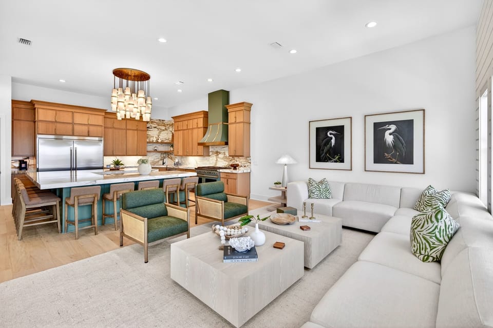 2nd floor - Spacious living room at Tony by the Sea designed for relaxing & group gatherings, featuring a large sectional, cane accent chairs, shiplap walls & oversized windows with palm tree views. Perfect for families vacationing in Miramar Beach, FL.
