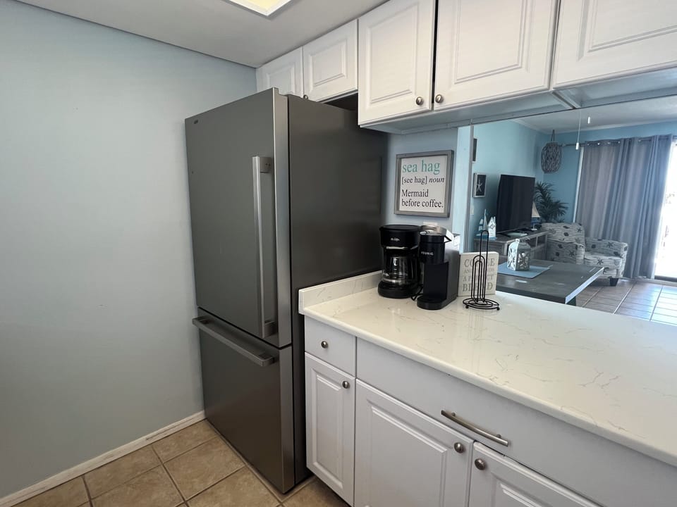 Your kitchen is ready for your morning coffee ritual, fully equipped with modern appliances and bright, welcoming cabinetry that opens to the inviting living space beyond.
