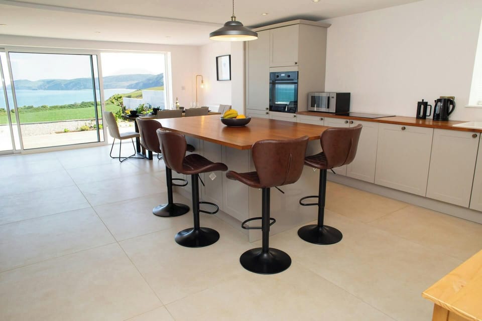 Kitchen-diner with central island, pendant light, and sea view through glass doors