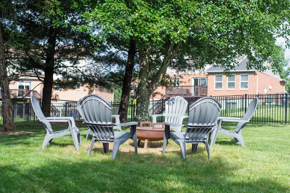 Shaded backyard fire pit with Adirondack seating and fenced lawn