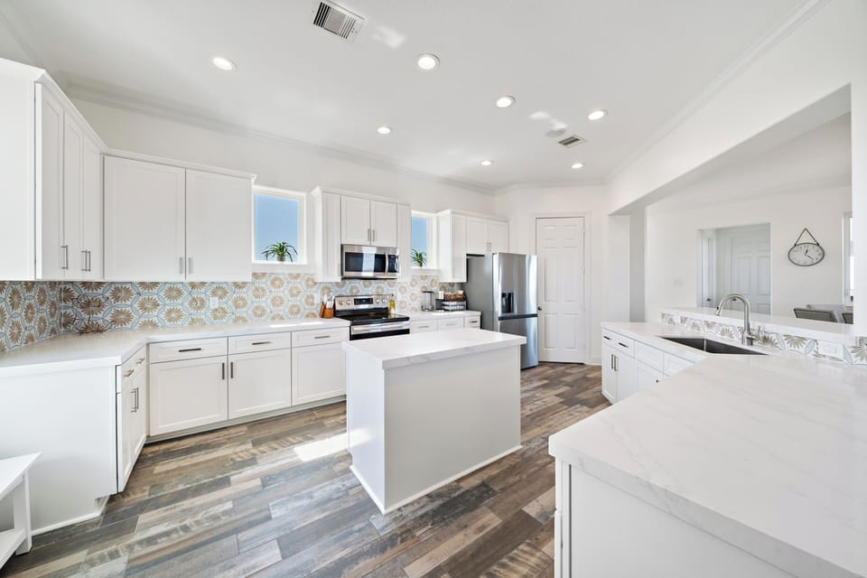 Spacious gourmet kitchen with oversized island, white cabinetry, recessed lighting, and open layout. Perfect for meal preparation and social gatherings.