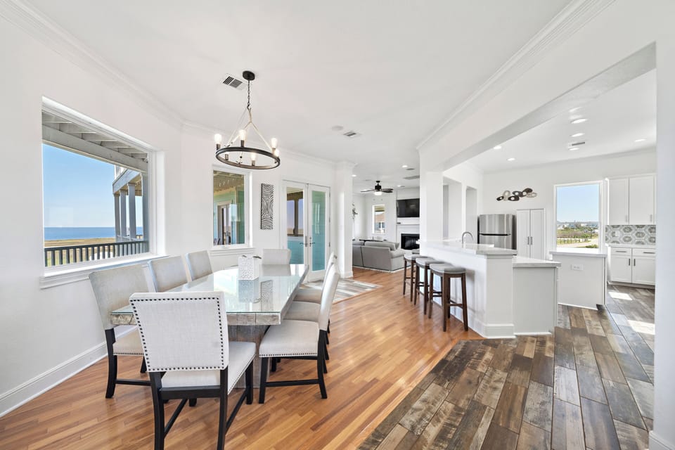 Open dining and living area featuring large windows, coastal views, hardwood flooring, and spacious seating. Ideal for entertaining and group vacations.